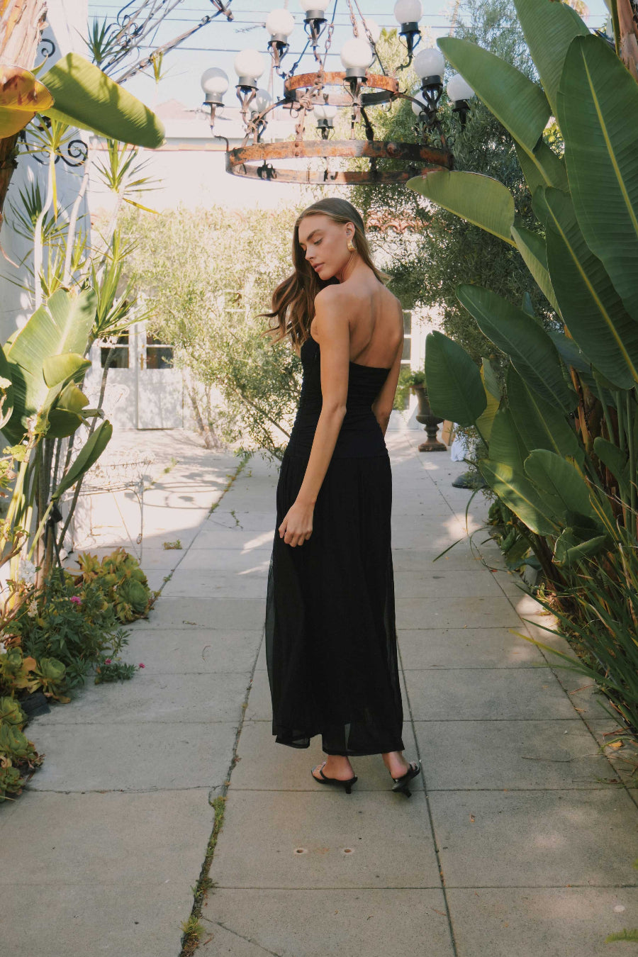 Woman in a black dress standing in a garden with plants and a stone path.
