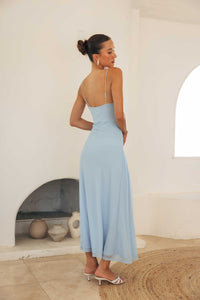 Woman in a light blue dress standing in a room with a white wall and arched window.