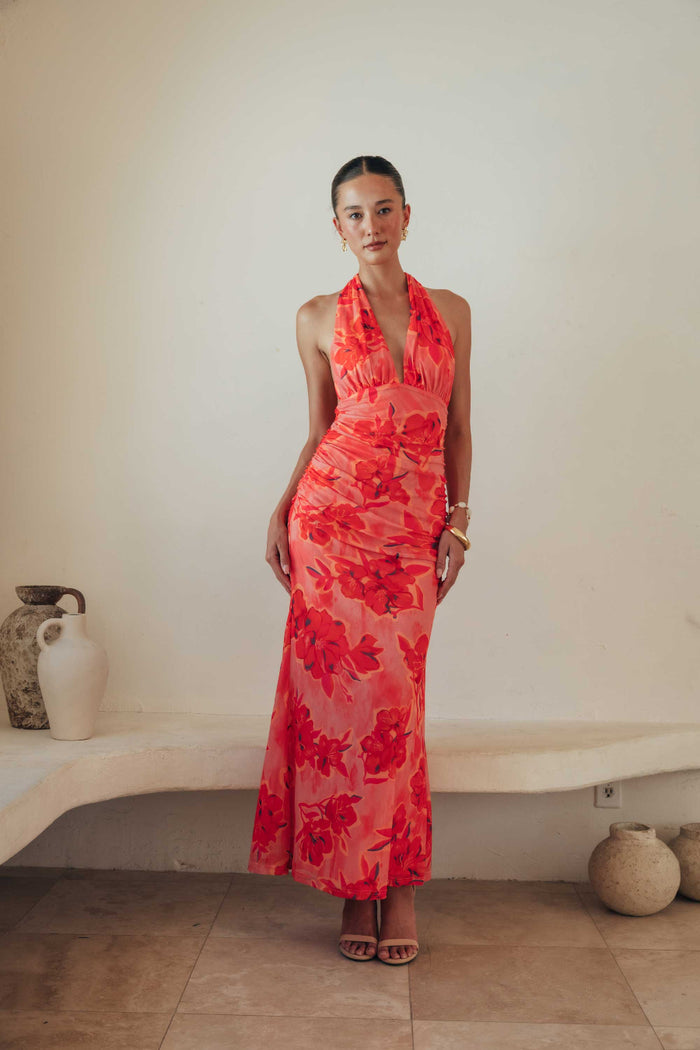 Woman wearing a coral floral dress standing against a plain wall.