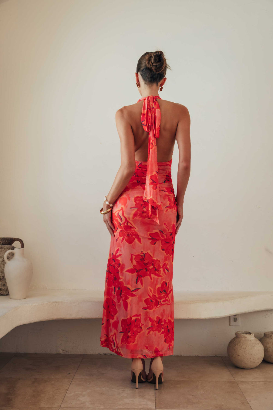 Woman wearing a red floral dress standing in a minimal indoor setting.