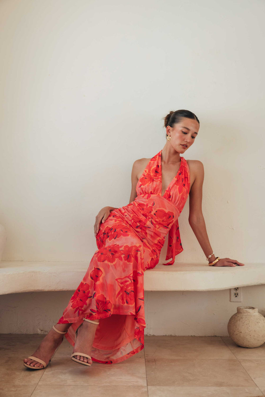 Woman in a red floral dress sitting on a white ledge.