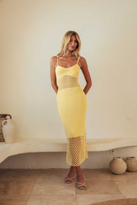 Woman wearing a yellow dress standing against a plain wall.