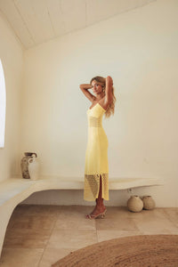 Woman in a yellow dress standing in a minimalistic room with white walls and a stone floor.