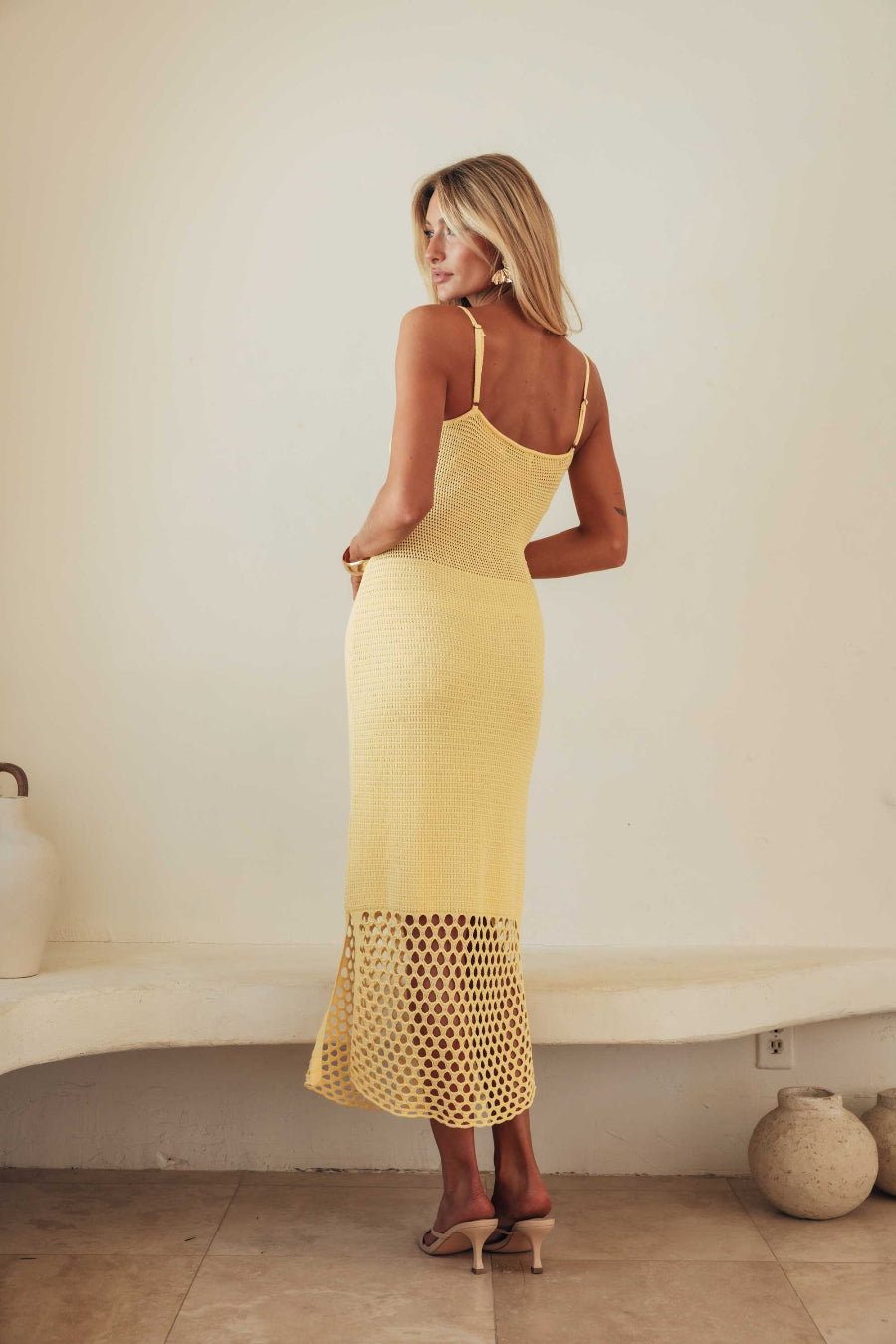 Woman wearing a yellow dress with a textured bottom half against a plain wall.
