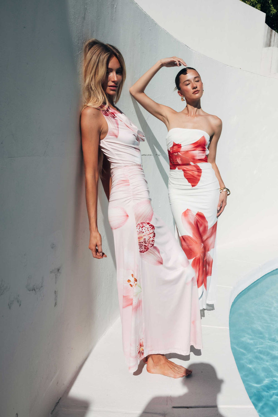 Two women wearing floral dresses standing by a poolside.