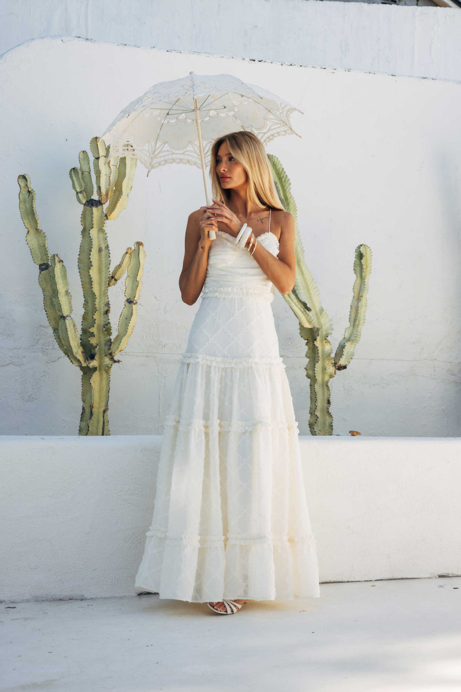Woman in a white dress holding an umbrella with cacti in the background