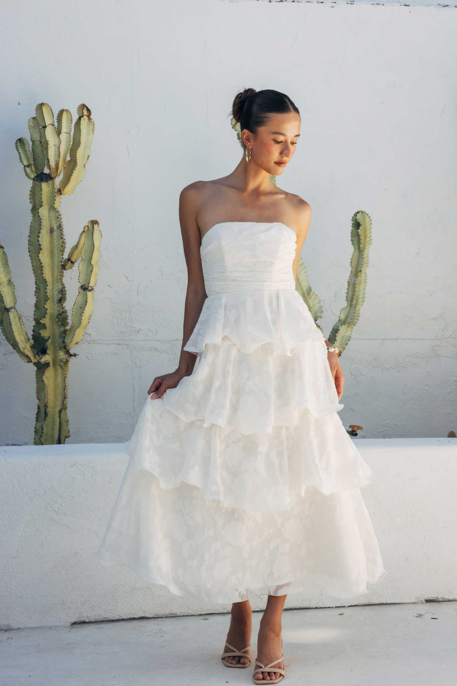 Woman in a white strapless dress standing in front of a cactus plant.