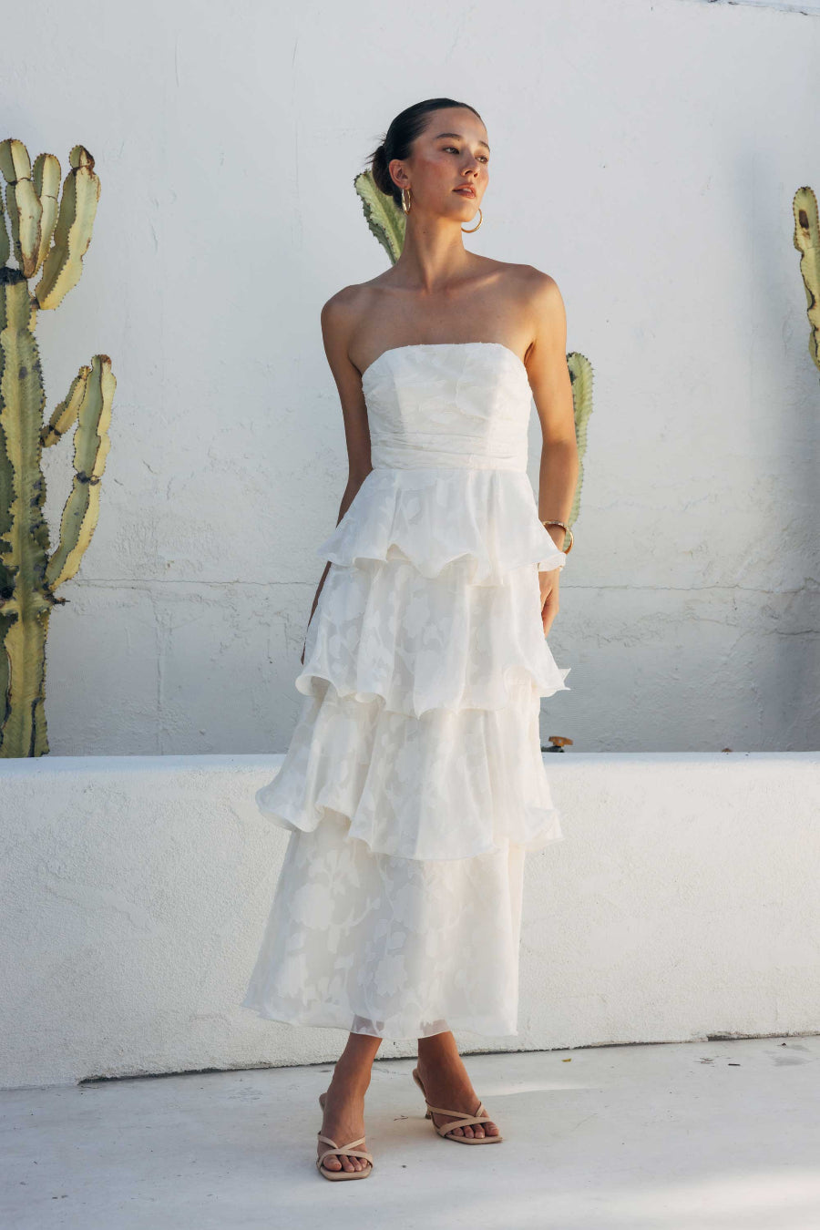 Woman in a white strapless dress standing against a white wall with cacti.