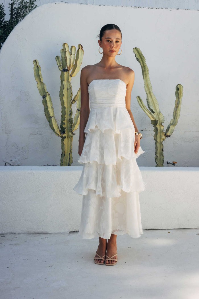 Woman in a white strapless dress standing in front of cacti against a white wall.
