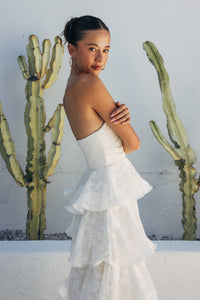 Woman in a white dress standing in front of cacti against a white wall