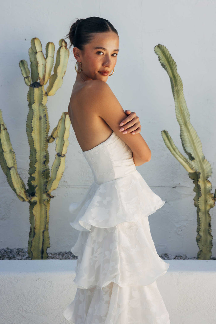 Woman in a white dress standing in front of cacti against a white wall