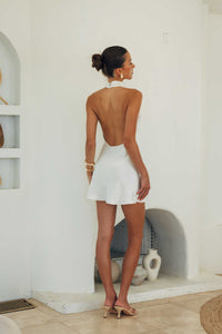 Woman in a white dress standing in a room with a white wall and decorative elements.