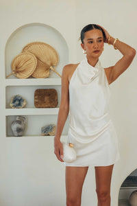 Woman in a white dress standing in a room with decorative items on shelves.
