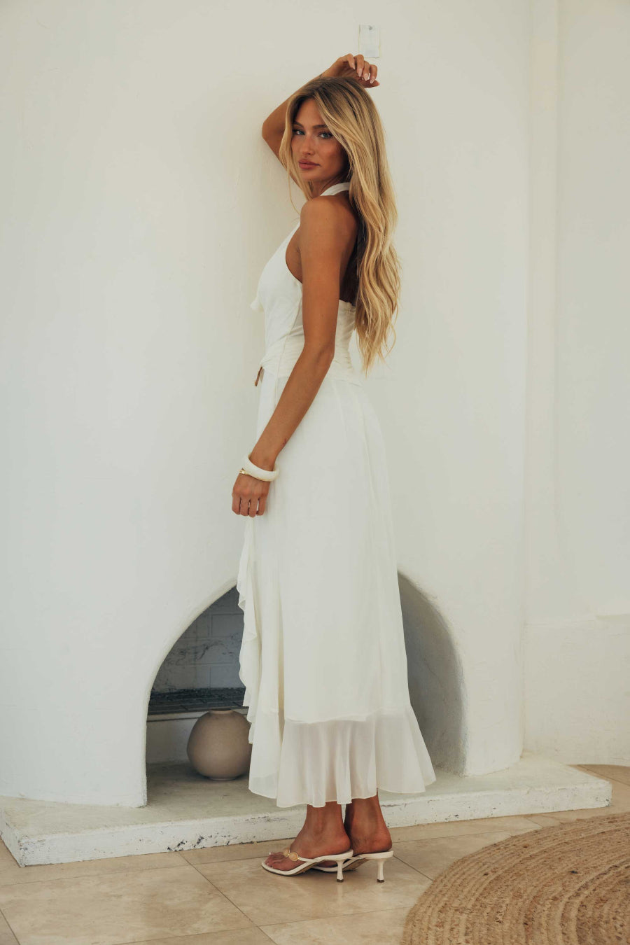 Woman in a white dress standing against a white wall.