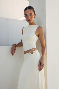 Woman wearing a white dress with a brown belt against a white wall.