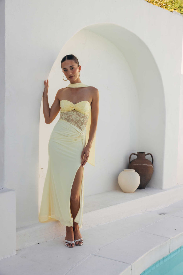 Woman in a yellow evening gown standing in a white architectural setting.