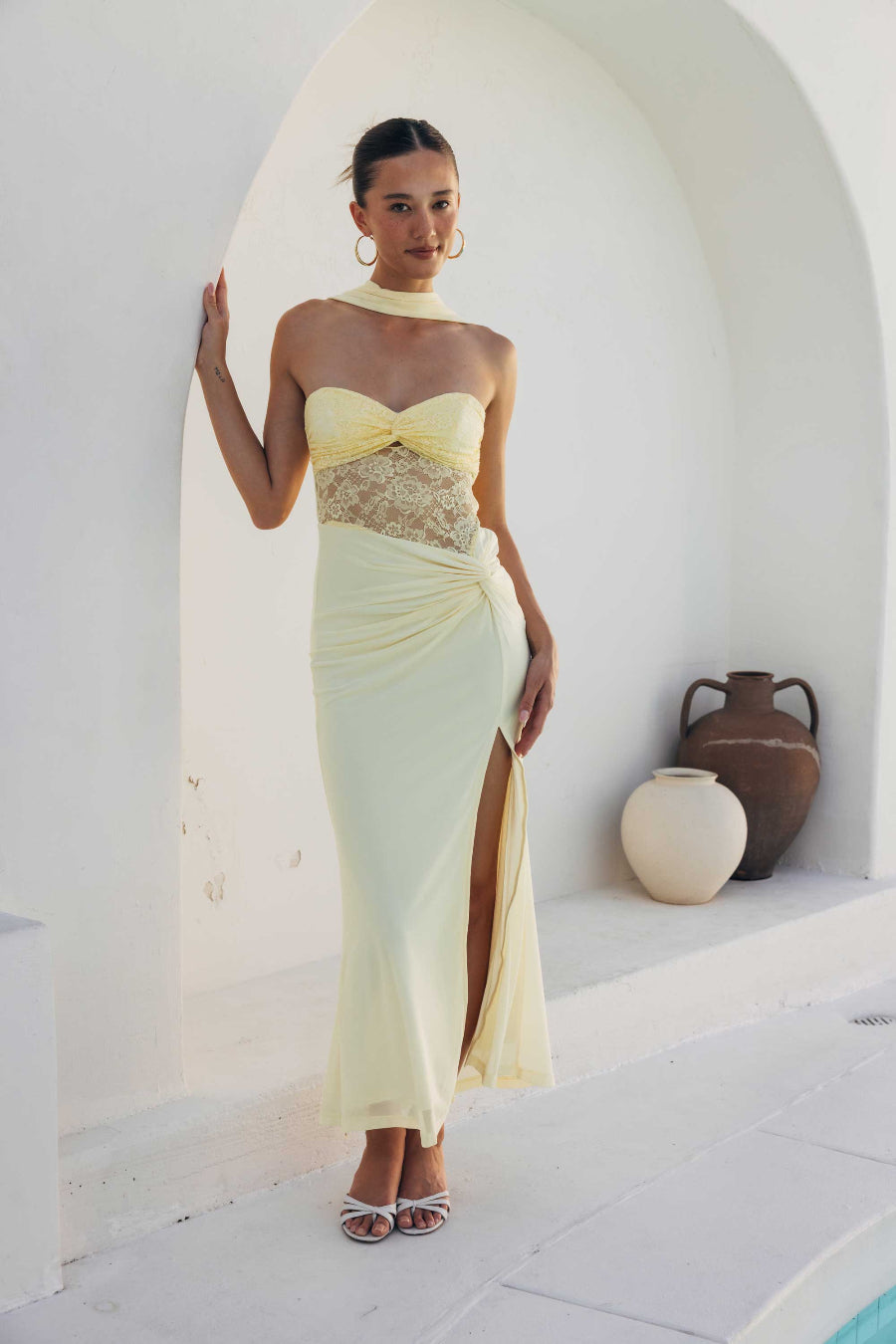 Woman in a strapless dress with a high slit standing in a sunlit outdoor setting.