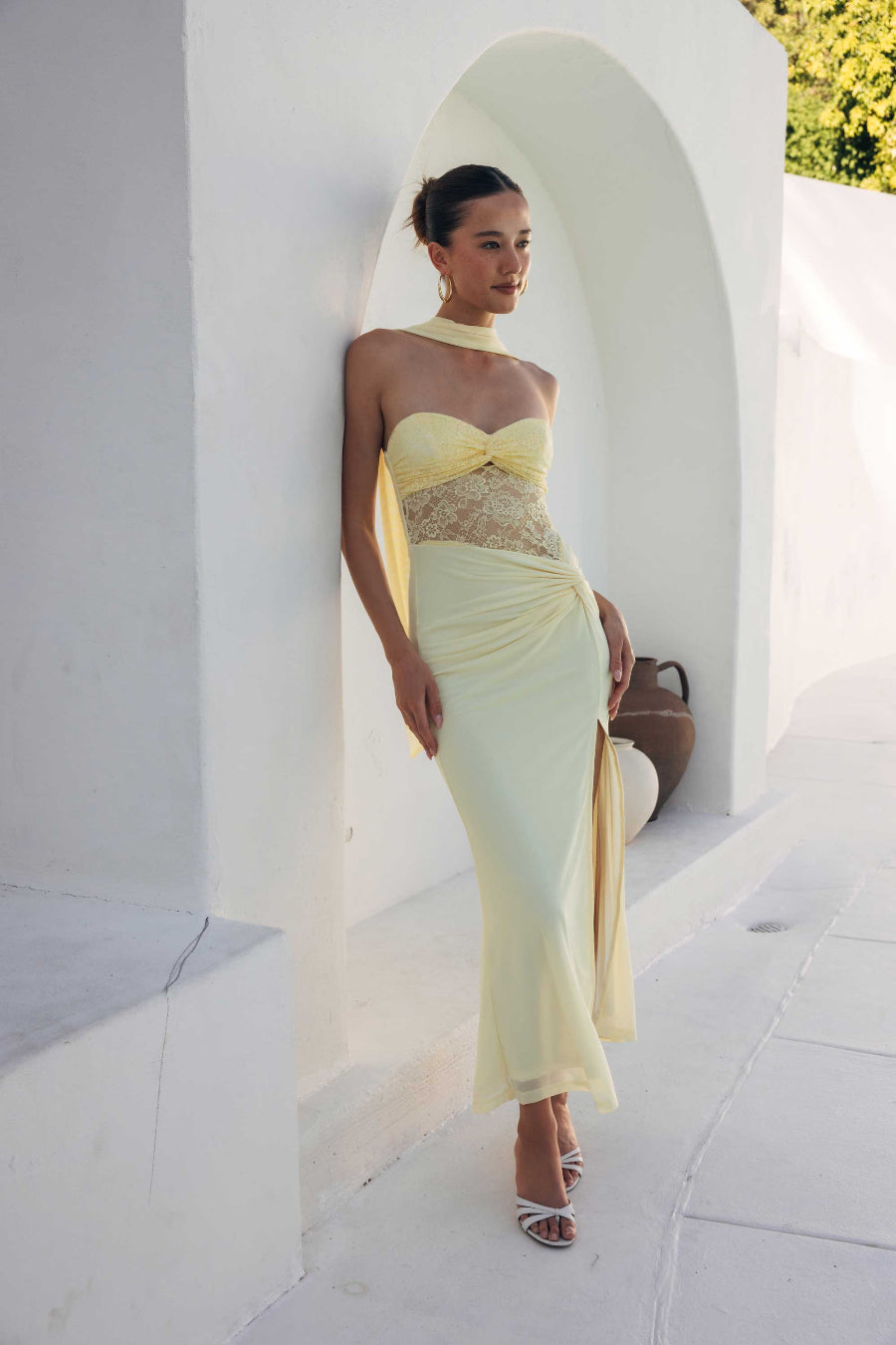Woman in a yellow evening gown standing against a white wall with arches.