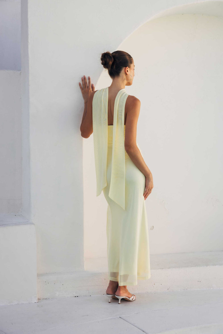 Woman in a light yellow dress standing against a white wall.