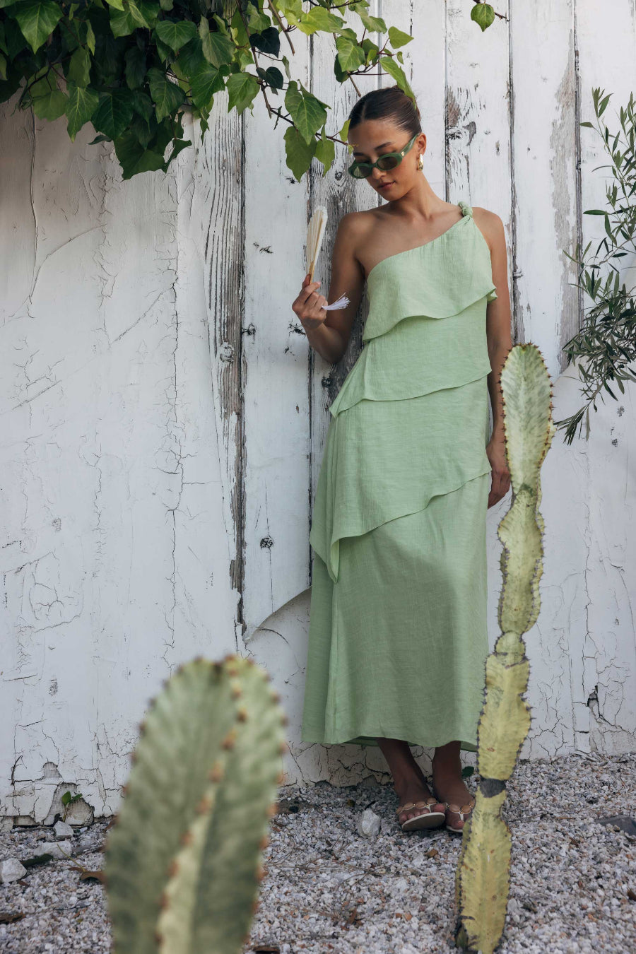 Woman in a green dress standing next to cacti against a white wall.