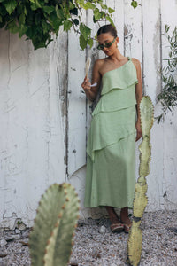 Woman in a green dress standing next to cacti against a white wall.