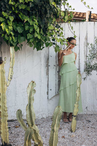 Woman in a light green dress standing among cacti and a white wooden fence.