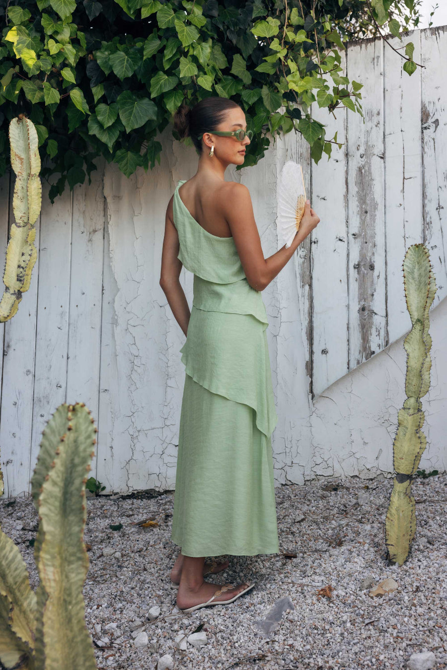 Woman in a light green dress standing in front of a white wooden fence with cacti around.