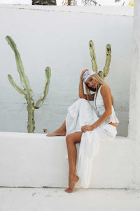 Woman in a white dress sitting against a white wall with cacti.