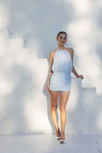 Woman in a light blue dress standing on white steps with a white wall background
