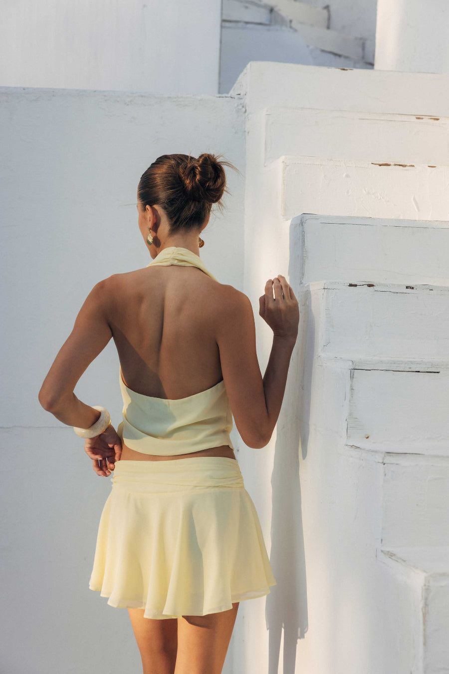 Woman in a light yellow dress standing against a white wall.
