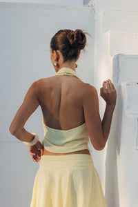 Woman in a light yellow dress standing against a white wall.
