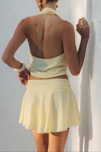 Woman in a light yellow dress standing against a white wall.