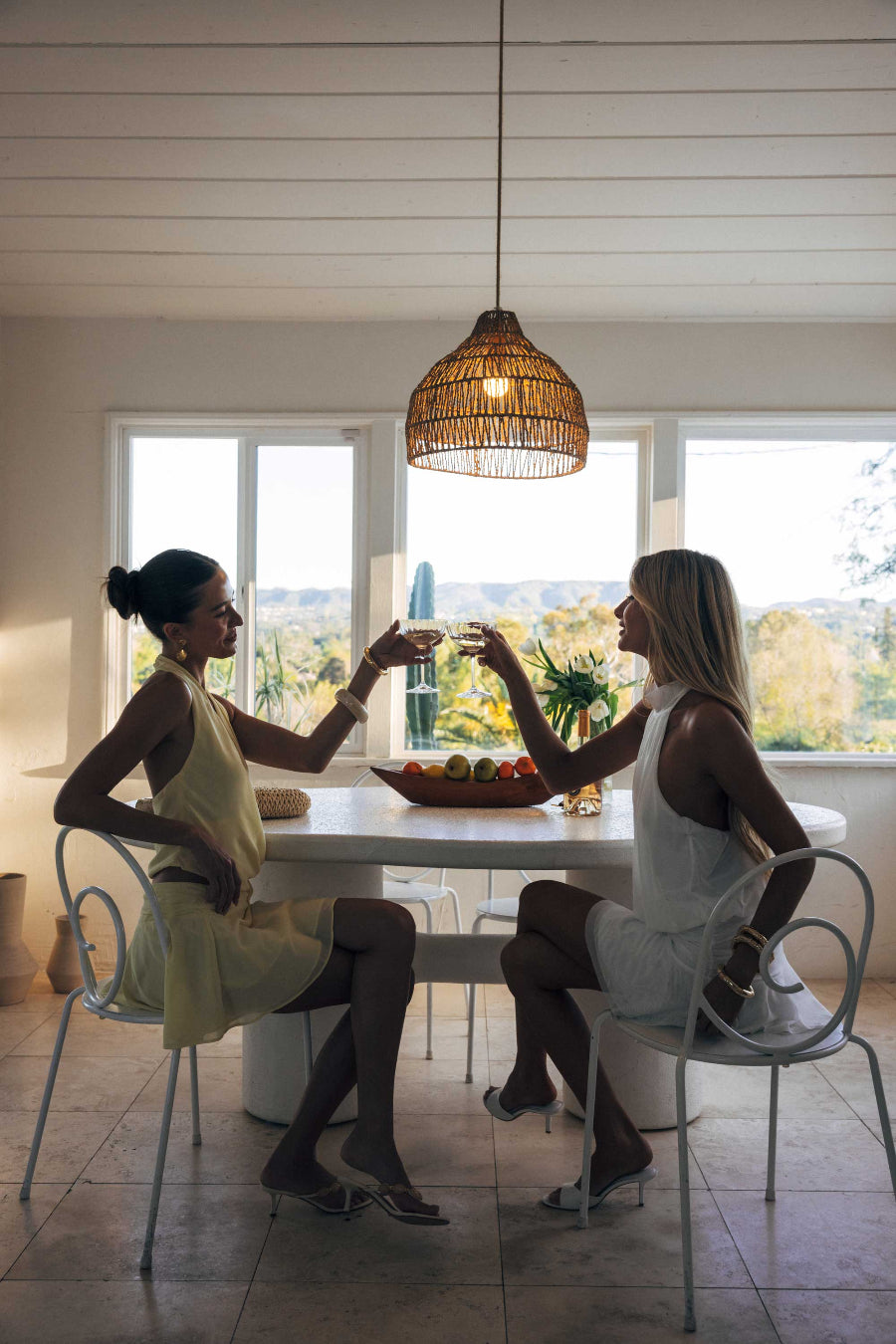 Two women sitting at a dining table in a bright room with large windows.