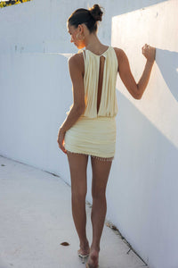Woman wearing a light yellow dress against a white wall