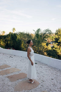 Woman in a white dress standing on a rooftop with greenery in the background