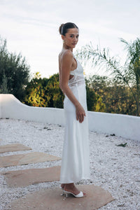 Woman in a white dress standing on a stone path with greenery in the background
