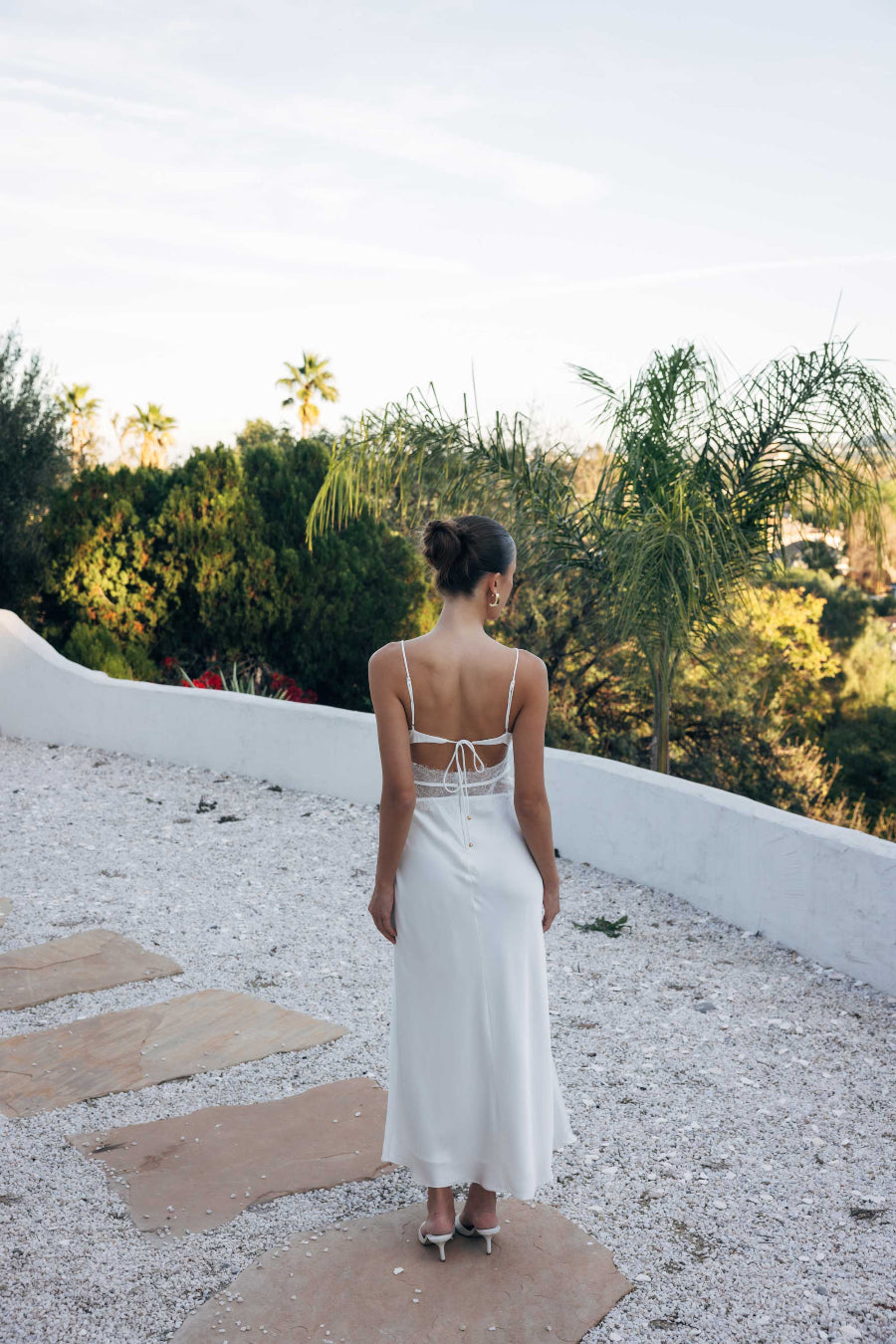 Woman in a white dress standing on a stone path with greenery in the background