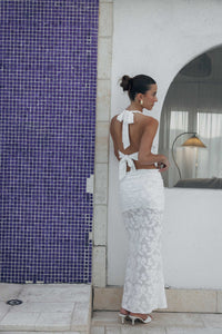 Woman in a white dress standing next to a blue tiled wall.