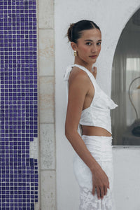 Woman in a white outfit standing against a tiled wall.