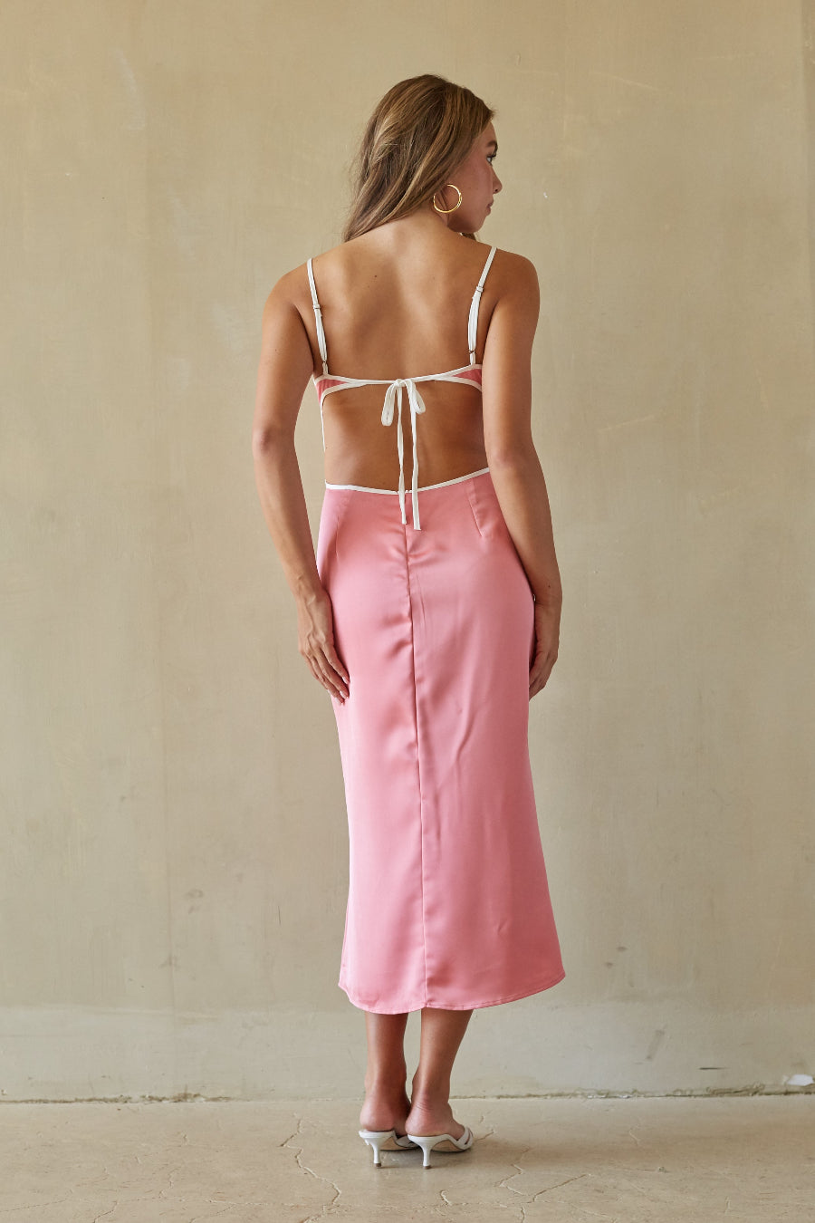 Woman wearing a pink skirt and white top against a beige wall.