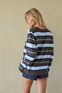 A woman wearing a striped knit sweater and denim shorts, photographed from the back against a plain beige wall.