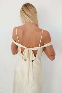 Woman wearing a cream-colored dress with thin straps and open back on a white background