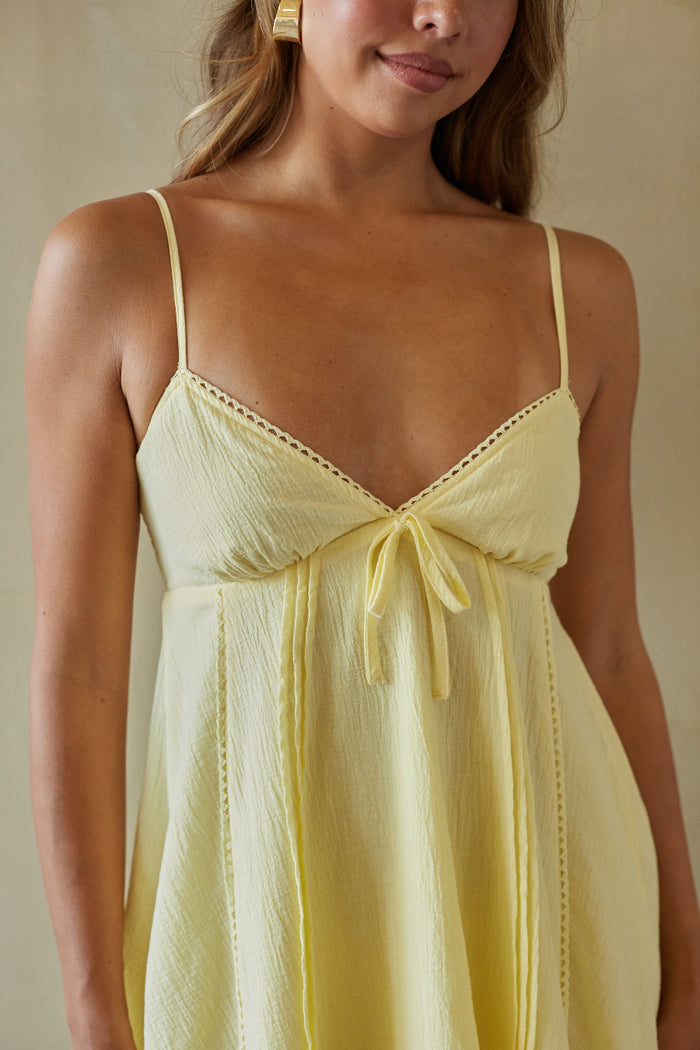Woman wearing a light yellow dress with thin straps against a neutral background