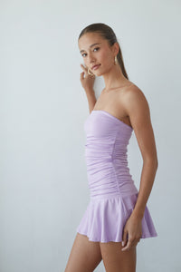 Woman wearing a strapless lavender dress against a plain background