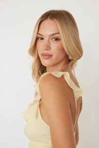 Woman wearing a light yellow dress with ruffled sleeves against a white background