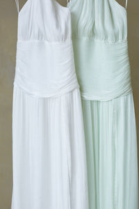 Two white dresses, one plain and one with a subtle pattern, on a beige background.