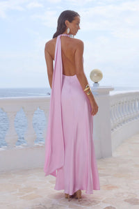 Woman in a pink dress standing on a balcony with ocean view