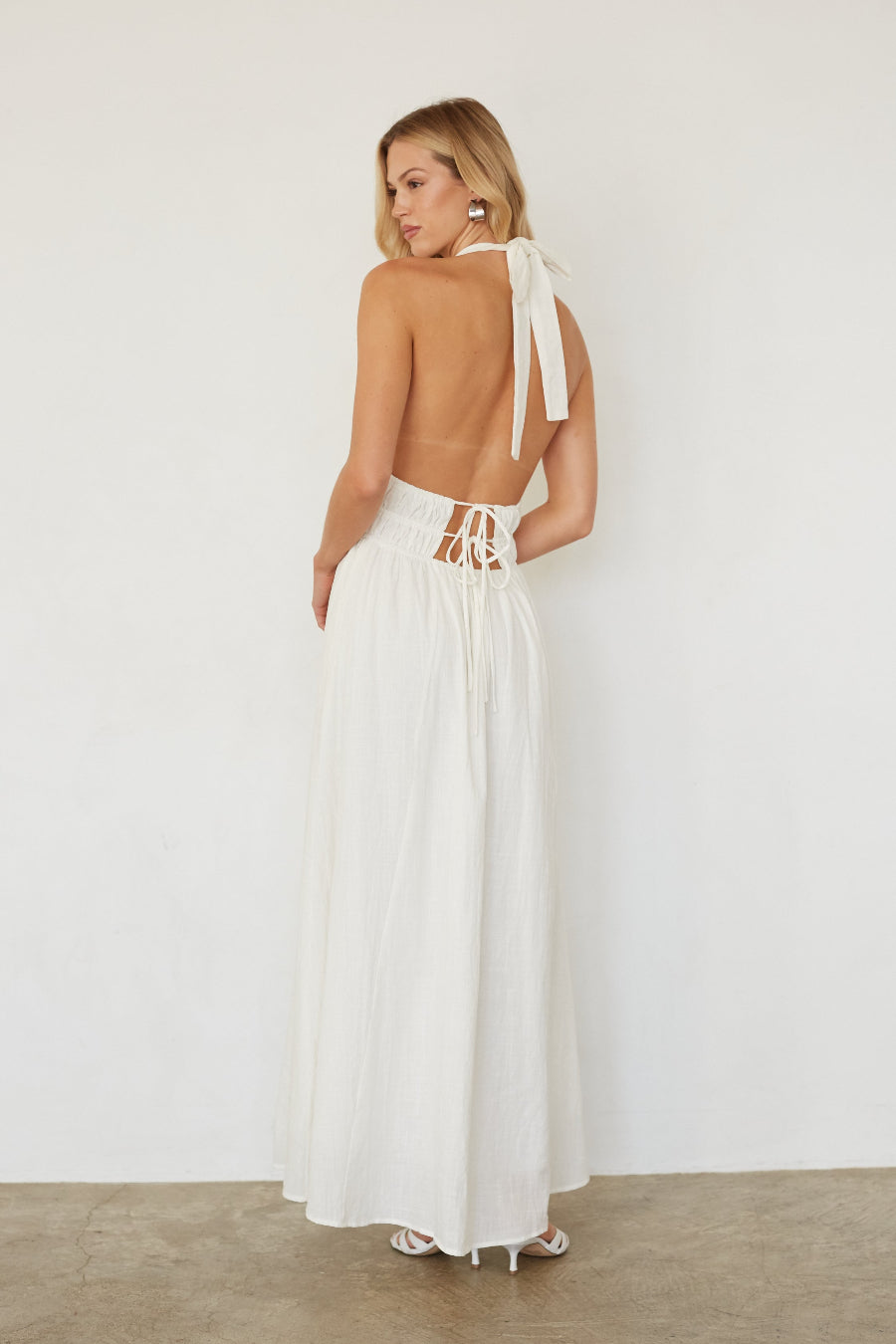 Woman wearing a white dress with cut-out back design on a plain background