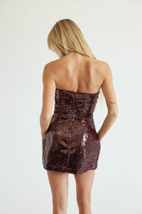 back of a women standing in front of a white wall in a maroon sparkly dress