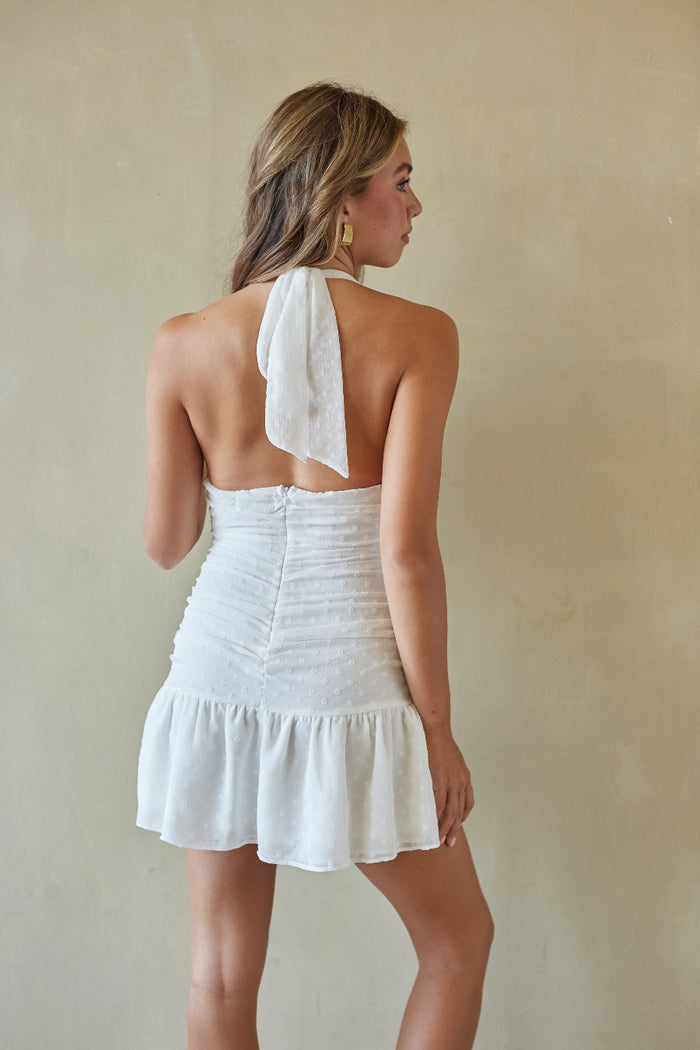 Woman wearing a white halter neck dress against a beige wall